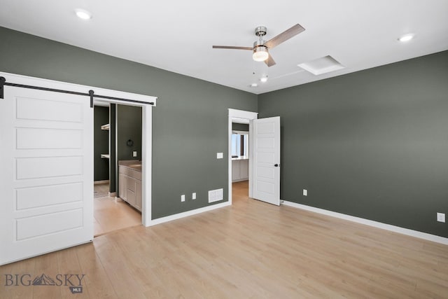 unfurnished bedroom featuring a barn door, light wood-type flooring, and ensuite bath