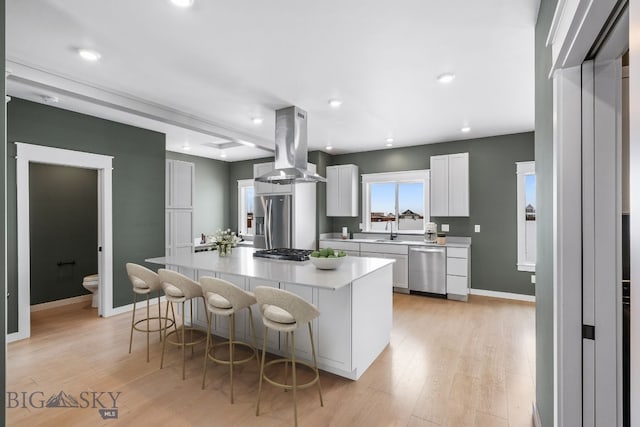 kitchen with a spacious island, a breakfast bar, white cabinetry, appliances with stainless steel finishes, and island exhaust hood