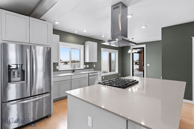 kitchen featuring sink, island range hood, appliances with stainless steel finishes, a kitchen island, and light hardwood / wood-style floors