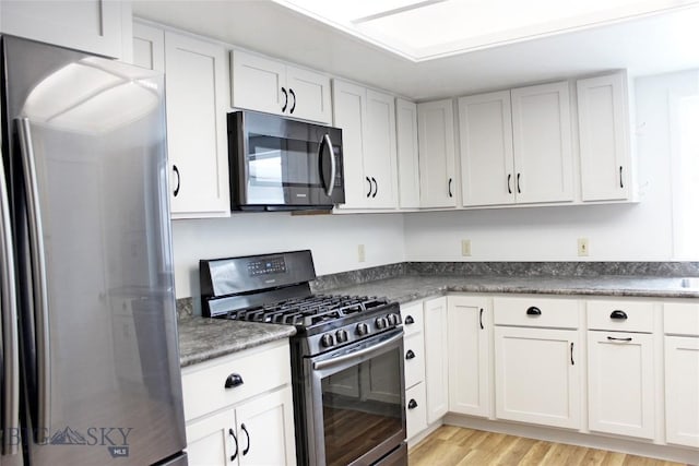 kitchen with stainless steel appliances, white cabinets, and light hardwood / wood-style floors