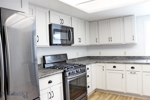 kitchen featuring dark countertops, white cabinetry, stainless steel appliances, and light wood finished floors