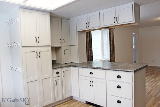 kitchen with white cabinetry, dark countertops, a peninsula, and light wood-type flooring