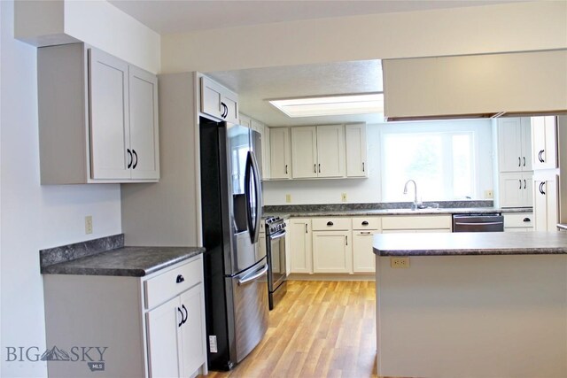 kitchen featuring light wood-type flooring, dark countertops, appliances with stainless steel finishes, and a sink