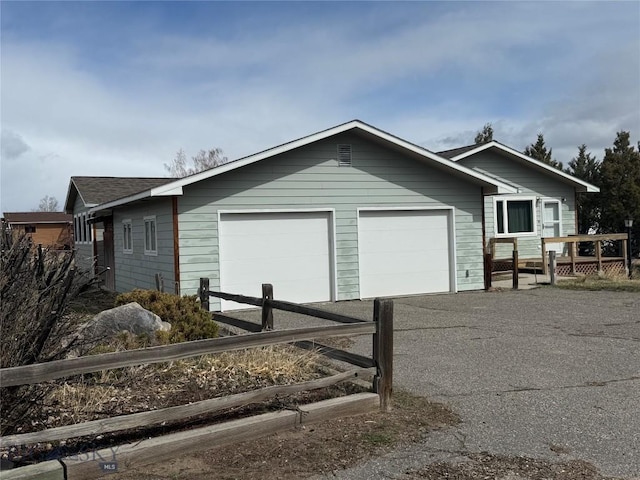 view of side of property with a garage, driveway, roof with shingles, a deck, and fence