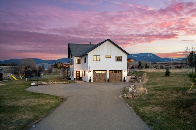 view of front of house featuring aphalt driveway, a trampoline, a yard, a mountain view, and board and batten siding