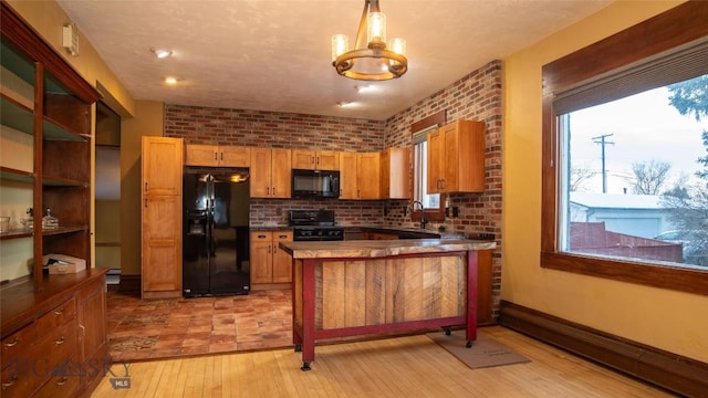 kitchen featuring brick wall, pendant lighting, black appliances, light hardwood / wood-style floors, and kitchen peninsula