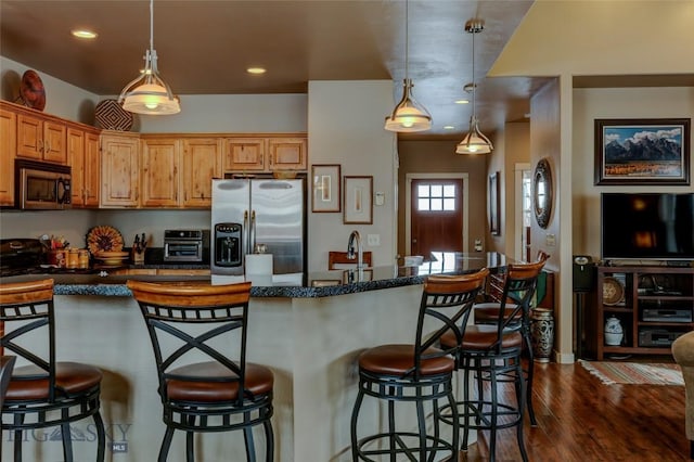 kitchen featuring a breakfast bar area, stainless steel appliances, a sink, dark wood finished floors, and decorative light fixtures