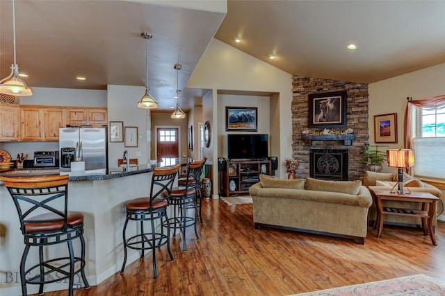 kitchen featuring a breakfast bar area, light wood-type flooring, a fireplace, and stainless steel fridge with ice dispenser