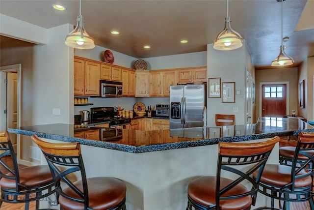 kitchen featuring appliances with stainless steel finishes, a breakfast bar area, dark stone countertops, hanging light fixtures, and recessed lighting