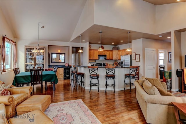 living room featuring baseboards, high vaulted ceiling, light wood finished floors, and a notable chandelier