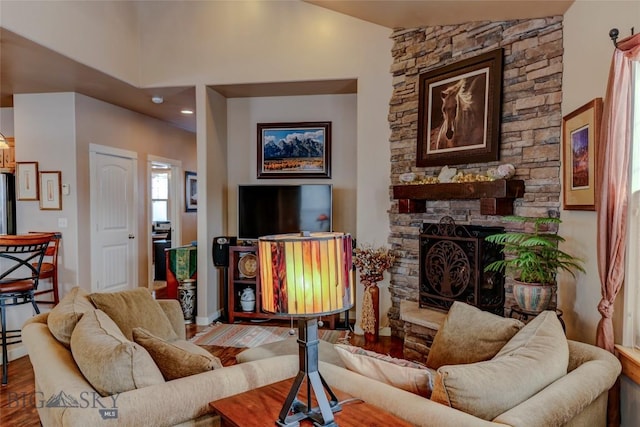 living area with vaulted ceiling, a stone fireplace, and wood finished floors