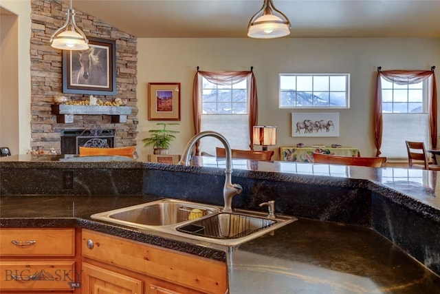 kitchen with hanging light fixtures, plenty of natural light, a stone fireplace, and a sink