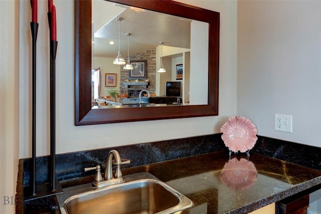 kitchen with vaulted ceiling, a stone fireplace, dark countertops, and a sink