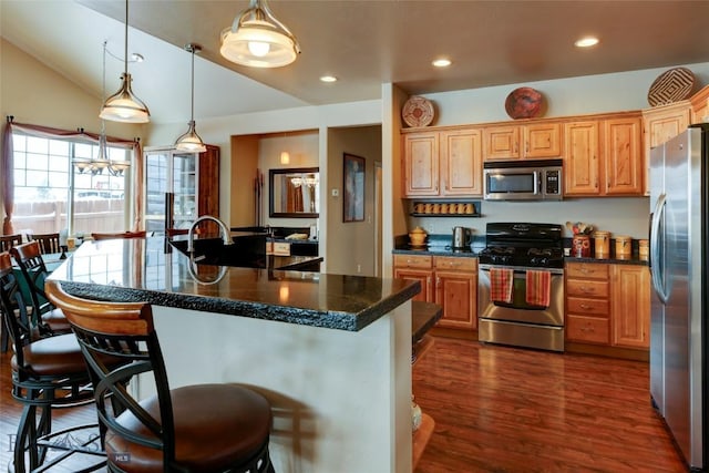 kitchen with appliances with stainless steel finishes, dark wood-style flooring, dark countertops, and a breakfast bar area