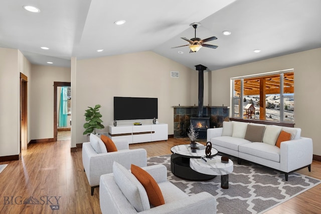 living room with vaulted ceiling, a wood stove, ceiling fan, and light wood-type flooring