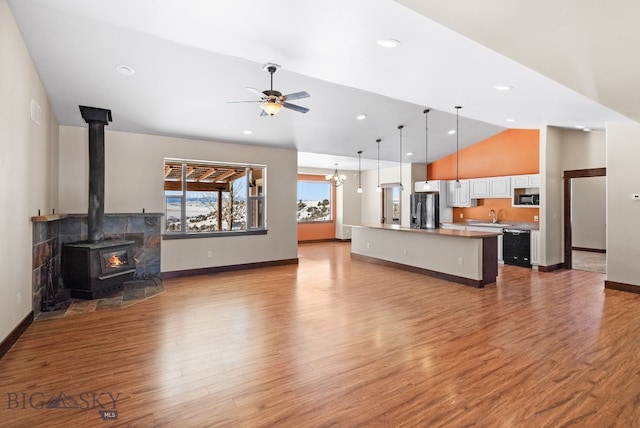 living room with lofted ceiling, a wood stove, ceiling fan with notable chandelier, and light wood-type flooring