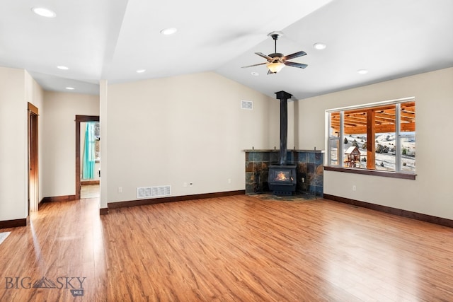 unfurnished living room with lofted ceiling, light wood-type flooring, ceiling fan, and a wood stove