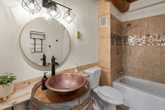 full bathroom featuring tiled shower / bath combo, sink, wood walls, and toilet