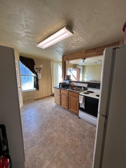 kitchen with baseboard heating, sink, white appliances, and wood walls