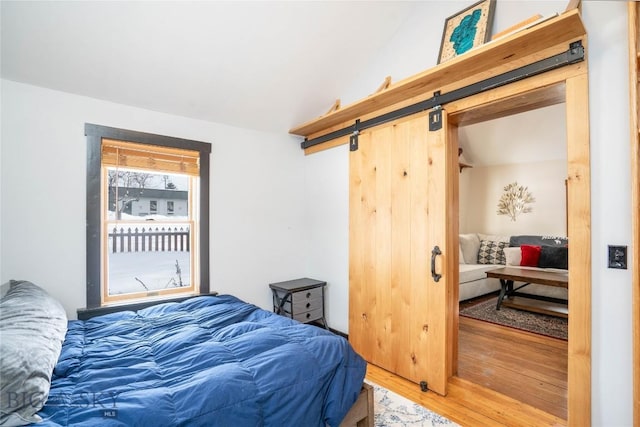 bedroom with lofted ceiling, hardwood / wood-style floors, and a barn door