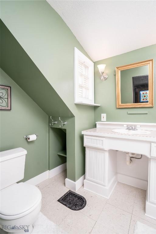 bathroom featuring lofted ceiling, sink, tile patterned floors, and toilet