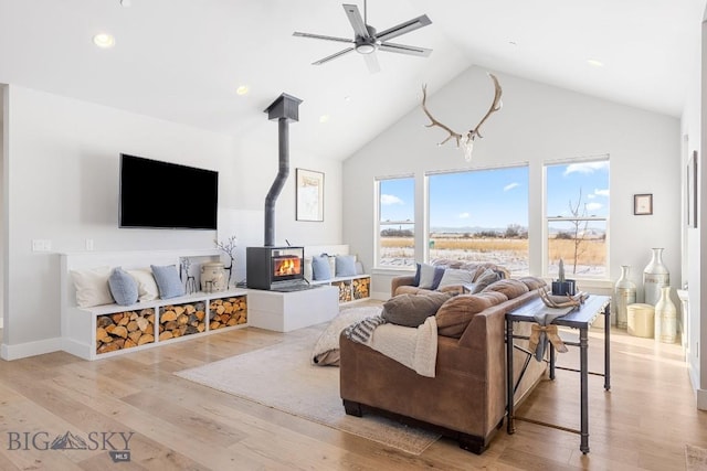 living room with ceiling fan, high vaulted ceiling, light hardwood / wood-style flooring, and a wood stove