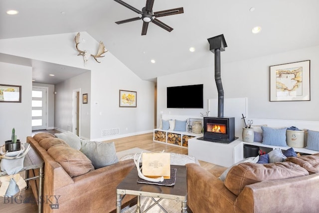 living room with ceiling fan, high vaulted ceiling, light hardwood / wood-style flooring, and a wood stove