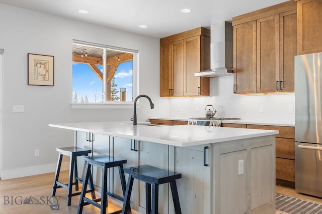 kitchen featuring a kitchen bar, wall chimney exhaust hood, sink, stainless steel fridge, and a kitchen island with sink