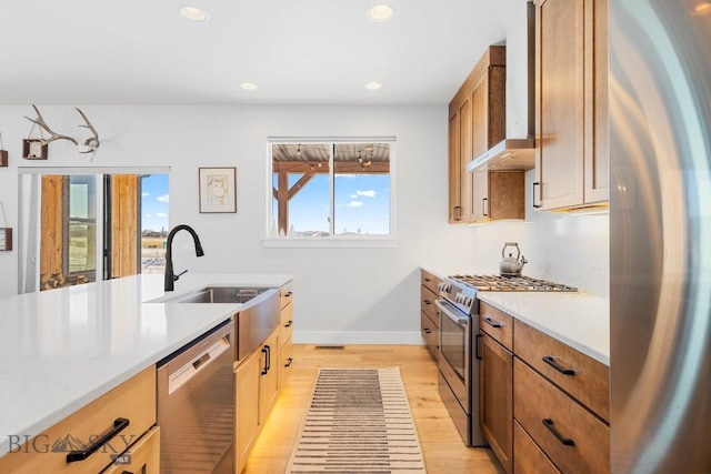 kitchen with stainless steel appliances, sink, wall chimney exhaust hood, and light hardwood / wood-style flooring