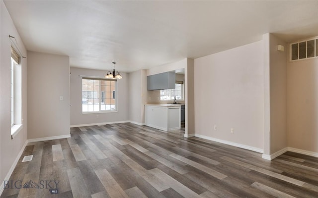 unfurnished living room with dark wood-type flooring, sink, and a notable chandelier