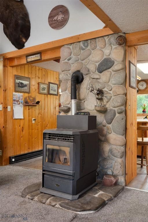 details featuring a baseboard heating unit, wooden walls, beamed ceiling, and a wood stove