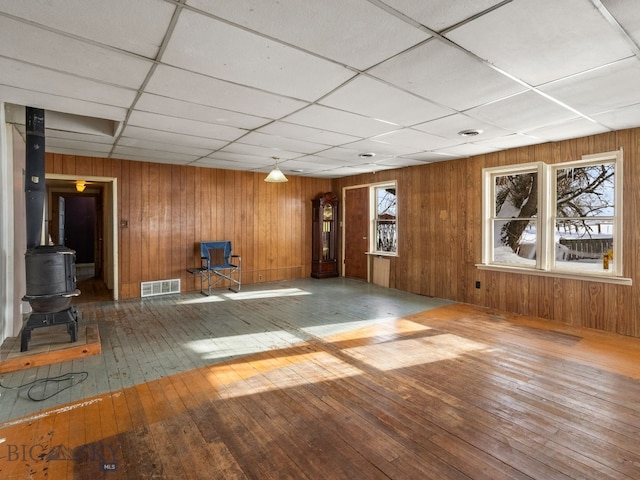 interior space featuring a paneled ceiling, a wood stove, hardwood / wood-style floors, and wooden walls