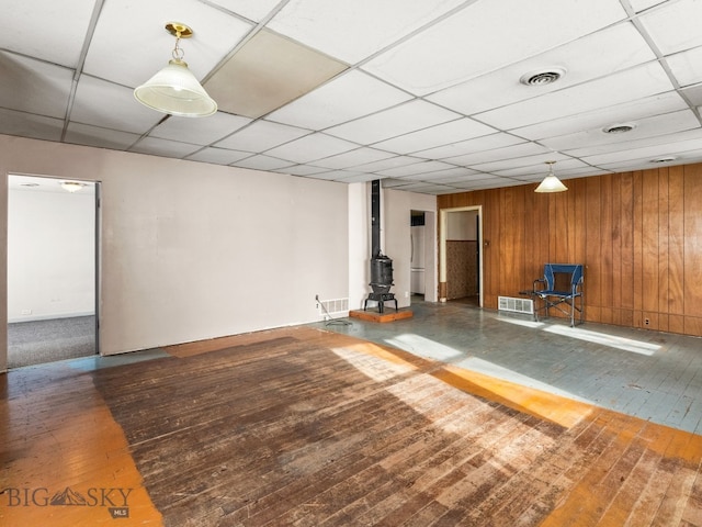 basement with hardwood / wood-style flooring, a paneled ceiling, wooden walls, and a wood stove