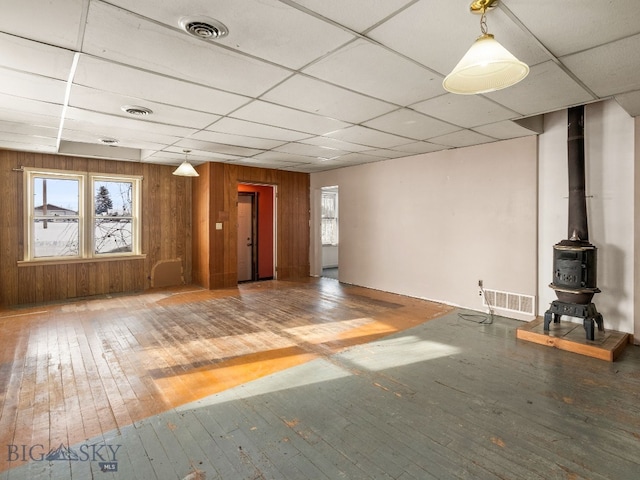 unfurnished living room featuring hardwood / wood-style flooring, a paneled ceiling, a wood stove, and wood walls