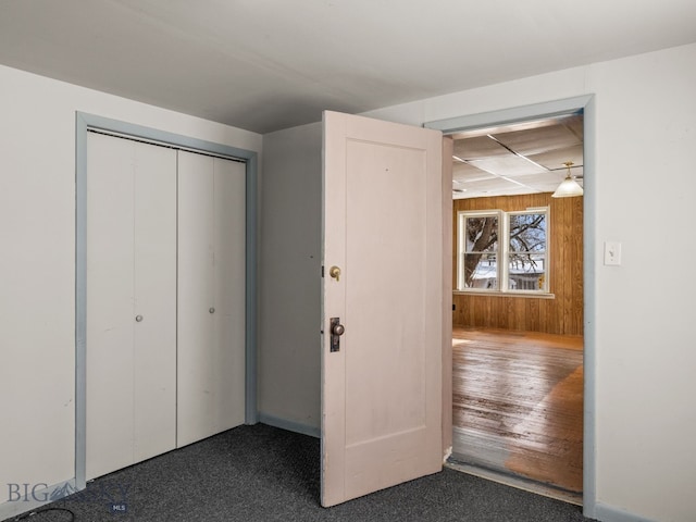 unfurnished bedroom featuring wooden walls, dark carpet, and a closet