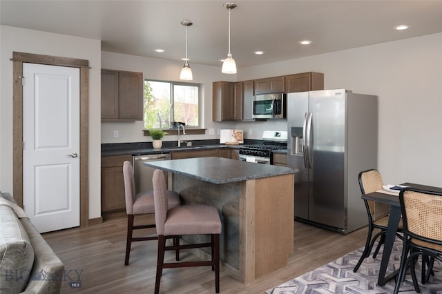 kitchen featuring sink, appliances with stainless steel finishes, hanging light fixtures, a kitchen island, and dark hardwood / wood-style flooring