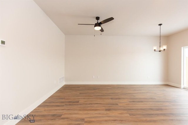 empty room featuring ceiling fan with notable chandelier and wood-type flooring