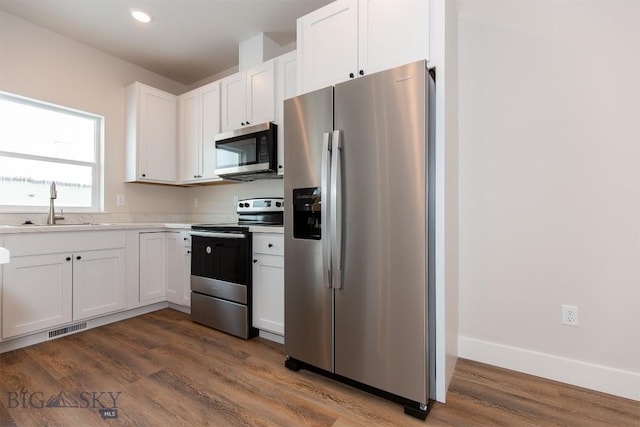 kitchen with dark wood-type flooring, stainless steel appliances, sink, and white cabinets