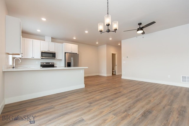 kitchen with appliances with stainless steel finishes, white cabinetry, hanging light fixtures, ceiling fan, and light hardwood / wood-style flooring