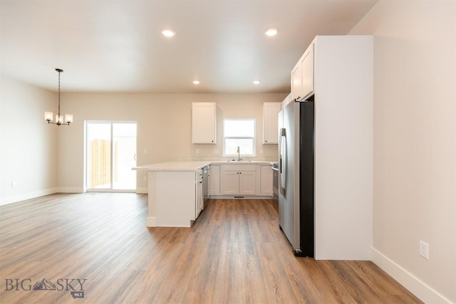 kitchen with white cabinetry, decorative light fixtures, kitchen peninsula, stainless steel appliances, and light hardwood / wood-style floors