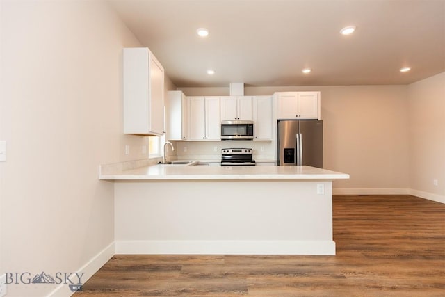 kitchen with sink, appliances with stainless steel finishes, hardwood / wood-style floors, white cabinets, and kitchen peninsula