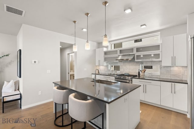 kitchen with sink, high end range, decorative backsplash, white cabinets, and decorative light fixtures