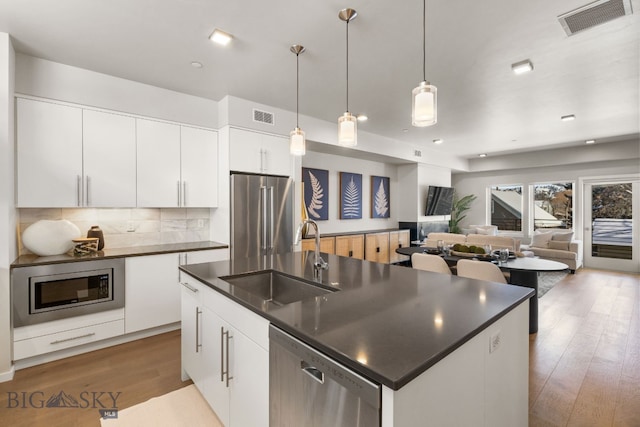 kitchen with pendant lighting, sink, stainless steel appliances, white cabinets, and a center island with sink