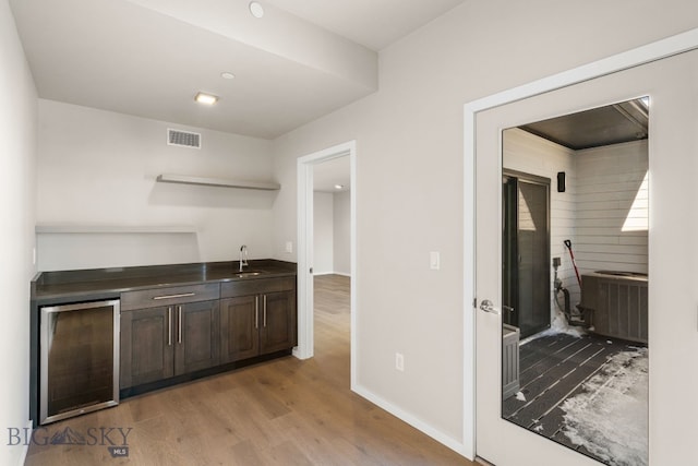 bar featuring wine cooler, sink, dark brown cabinets, and light hardwood / wood-style flooring