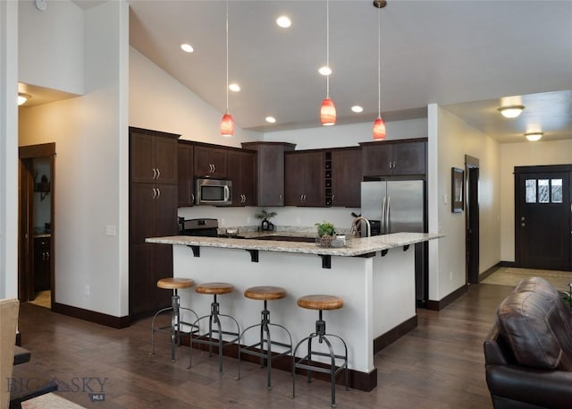 kitchen with appliances with stainless steel finishes, a breakfast bar, decorative light fixtures, a kitchen island with sink, and light stone countertops