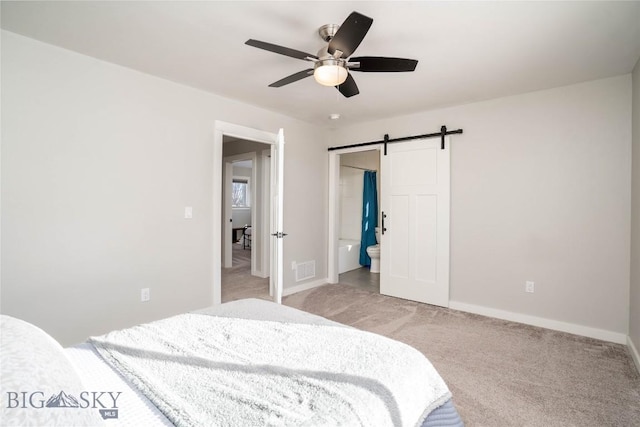 carpeted bedroom with a barn door, connected bathroom, and ceiling fan