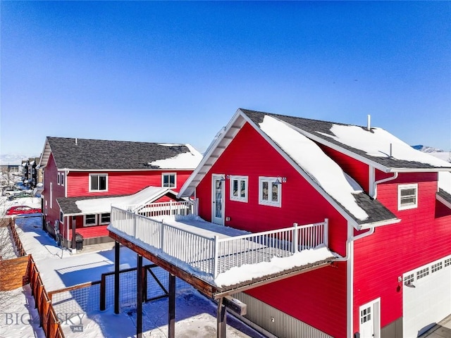 snow covered rear of property featuring a garage and a deck