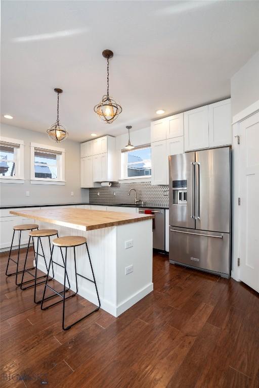 kitchen with butcher block countertops, decorative light fixtures, appliances with stainless steel finishes, decorative backsplash, and white cabinets