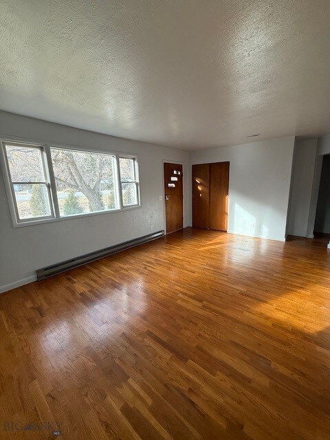 5042 US Highway 89 S, Livingston, MT 59047 - unfurnished living room with light wood-type flooring, a textured ceiling, a baseboard radiator, and baseboards