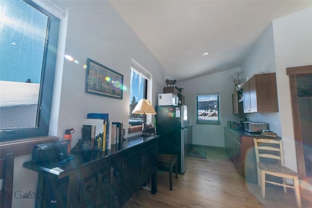 kitchen featuring stainless steel refrigerator, light hardwood / wood-style floors, and vaulted ceiling